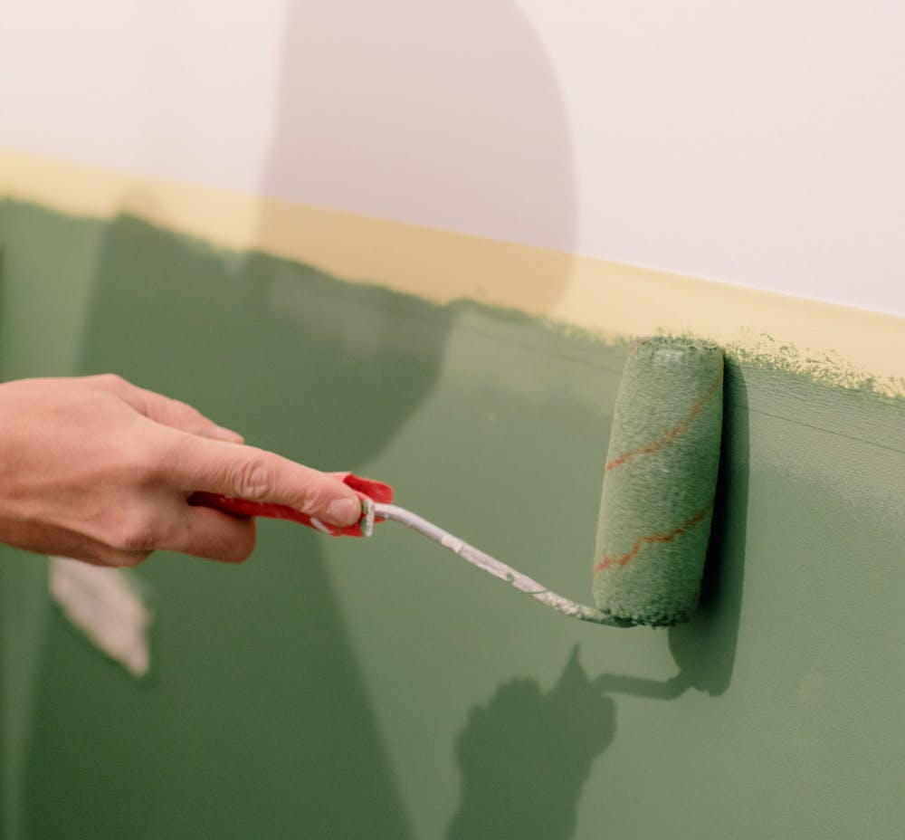 Main de femme qui peint un mur avec un rouleau de peinture verte